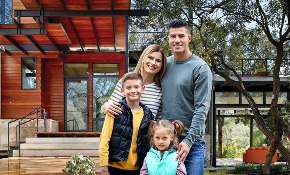 Southlake family of four smiling in front of home with custom iron doors and windows