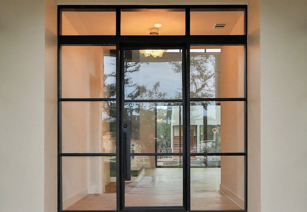 Large square top front door surrounded by large windows with minimal iron framing