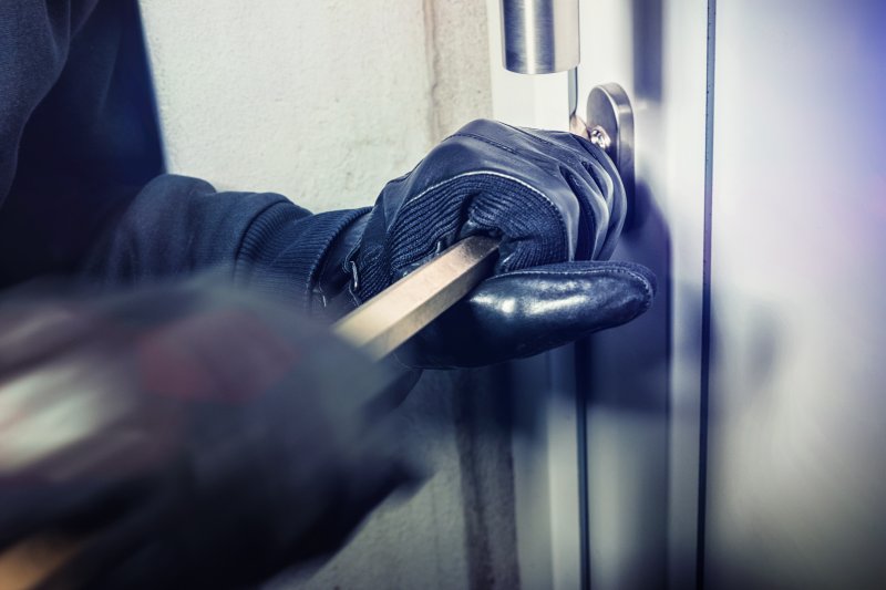 an up-close view of a person using a crowbar to try and break through the door of a home